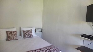 A hotel room with a bed, two decorative pillows, a bedside table, and a mounted TV.