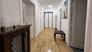 A hallway with wooden flooring, white walls, and a black bench. There are doors on both sides and a coat rack in the center. - ADORABLE two-bedroom apartment close to Vatican City (Roma)