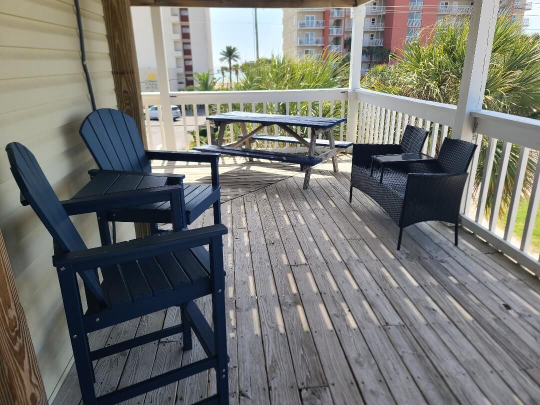 Een houten terras met tuinmeubilair, waaronder stoelen en een tafel, met uitzicht op een woongebied met gebouwen en groen.