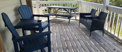 Een houten terras met tuinmeubilair, waaronder stoelen en een tafel, met uitzicht op een woongebied met gebouwen en groen.