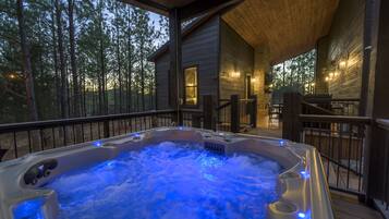 A wooden cabin with a hot tub on the porch, surrounded by trees.