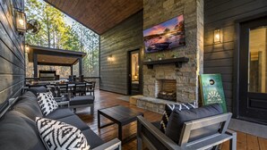 A cozy outdoor seating area with a stone fireplace, wooden furniture, and a TV mounted on the wall.