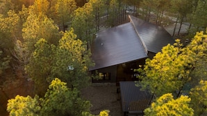 A modern cabin with a sloped roof surrounded by dense forest, viewed from an elevated angle during sunset.