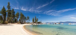 Ein Strand mit klarem türkisblauem Wasser, sandigem Ufer und hohen Kiefern.