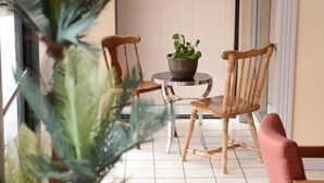 Una habitación con una silla de madera, una pequeña mesa con una planta en maceta y una silla roja.
