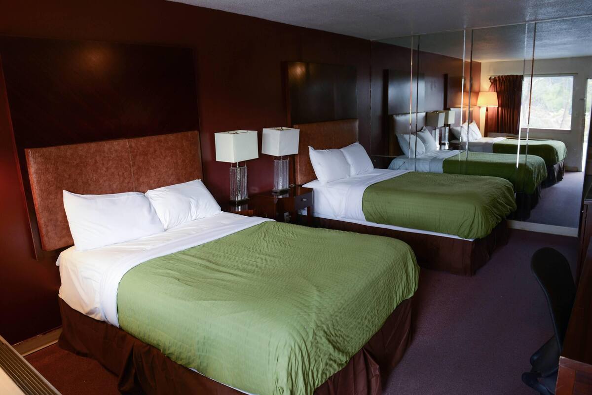 A hotel room with two beds, each with green bedding, a large mirror, and bedside lamps.