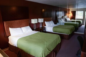 A hotel room with two beds, each with green bedding, a large mirror, and bedside lamps.