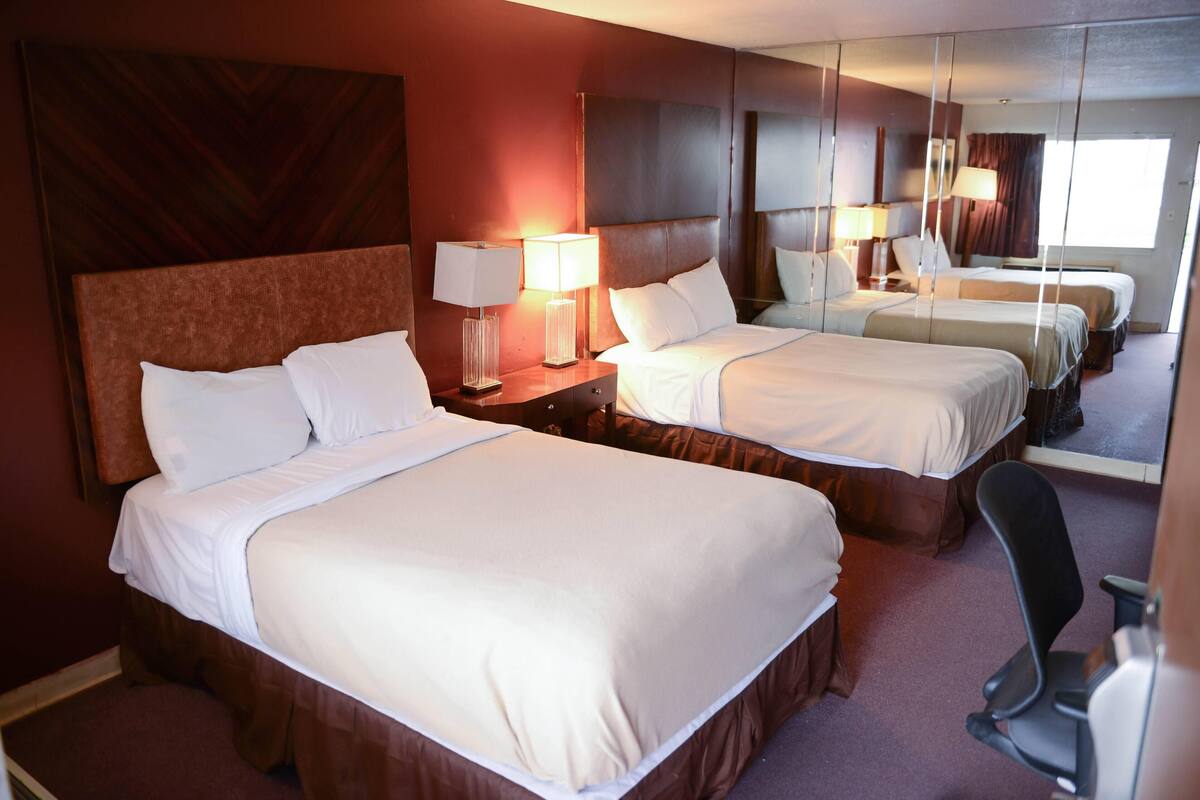 A hotel room with two beds, a large mirror, and a chair.
