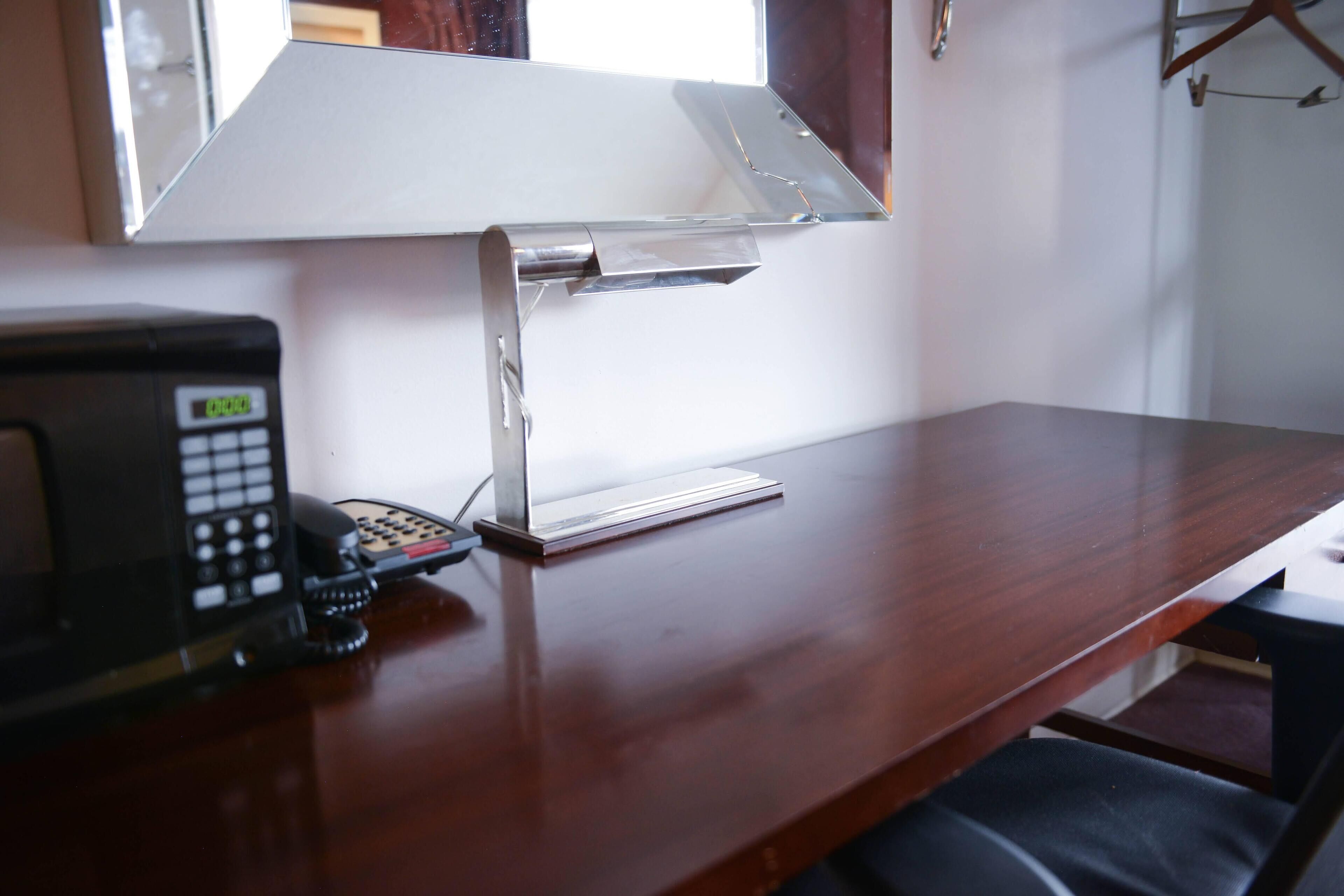 A wooden desk with a telephone, a lamp, and a chair.