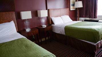 A hotel room with two beds, each with a green bedspread and white linens, a wooden headboard, and a nightstand with a lamp.
