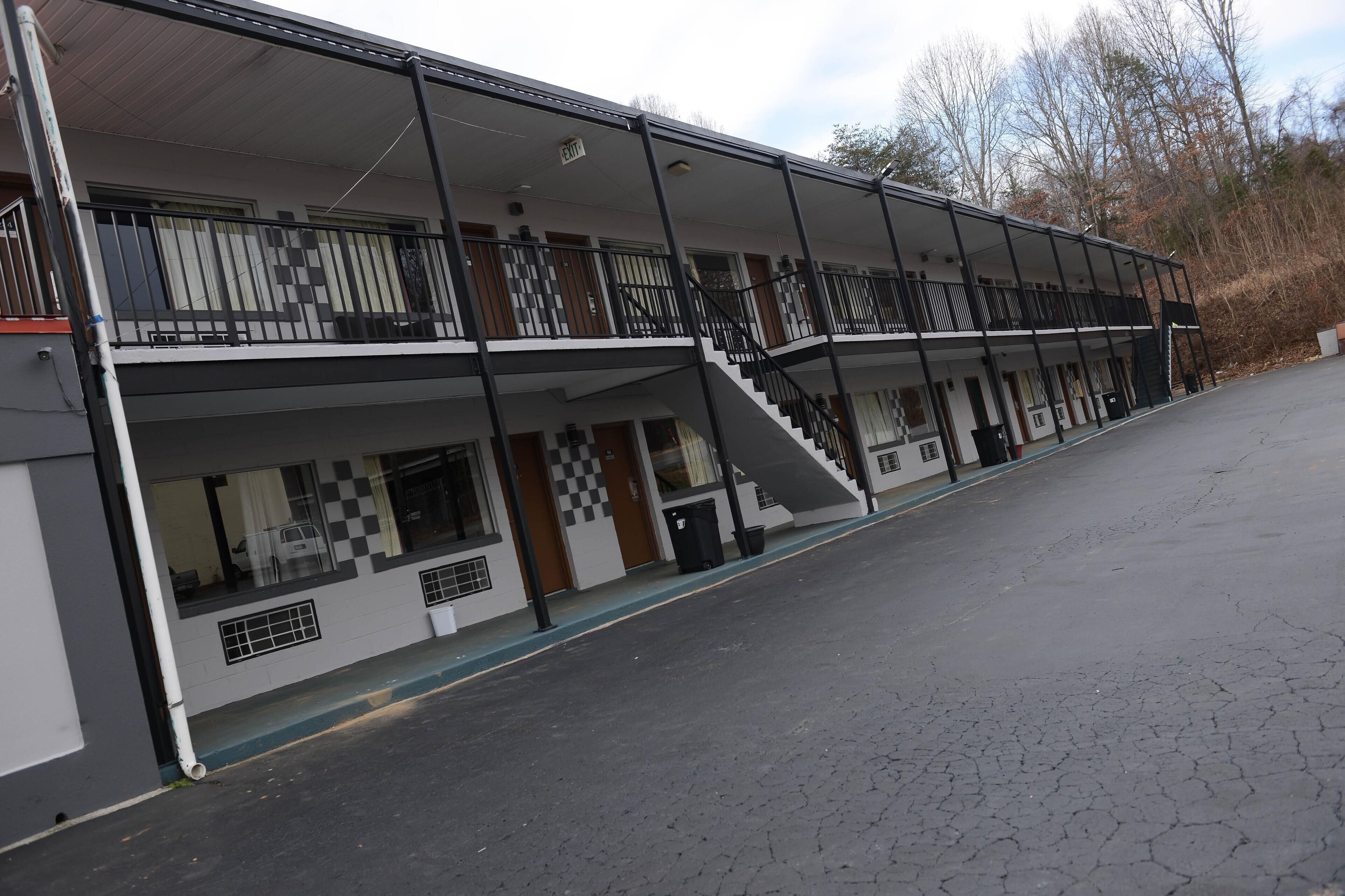 A two-story motel with a balcony on the upper floor, a staircase leading to the entrance, and a parking lot in front.