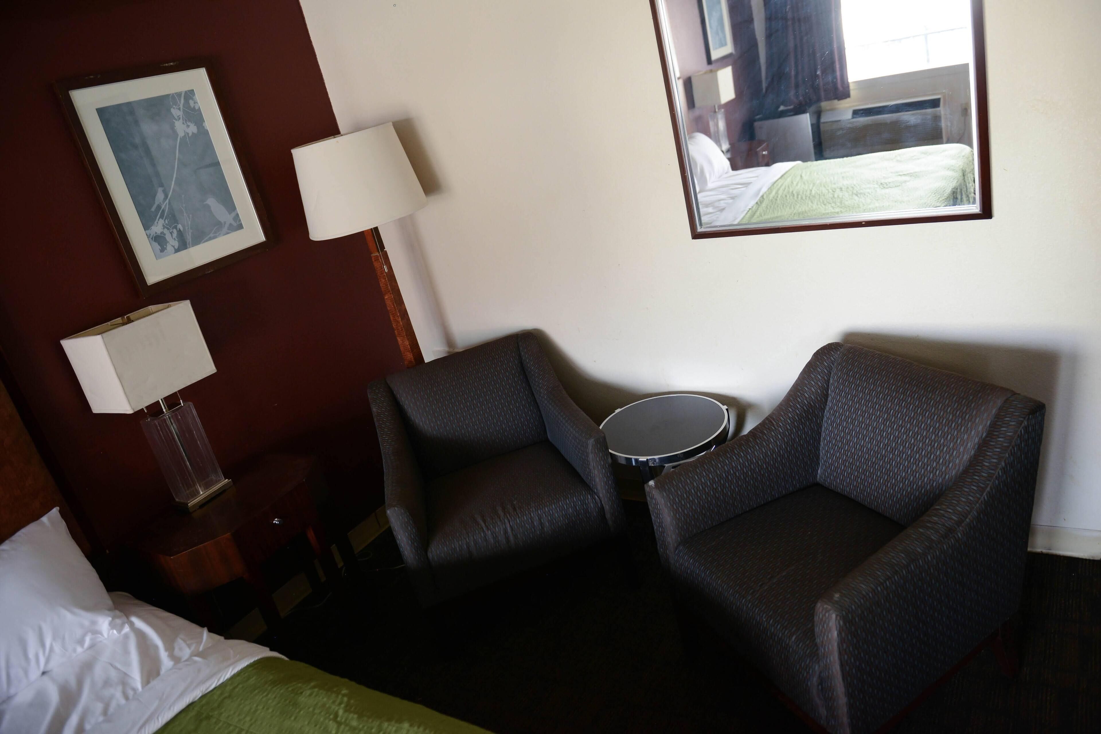 A hotel room with a bed, two armchairs, a small table, a lamp, and a framed picture on the wall.