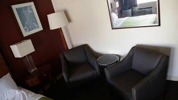 A hotel room with a bed, two armchairs, a small table, a lamp, and a framed picture on the wall.