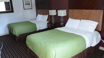 Camera d'albergo con due letti, ognuno con copripiumino verde e lenzuola bianche, una testiera in legno, un comodino con due lampade e un tappeto a righe.