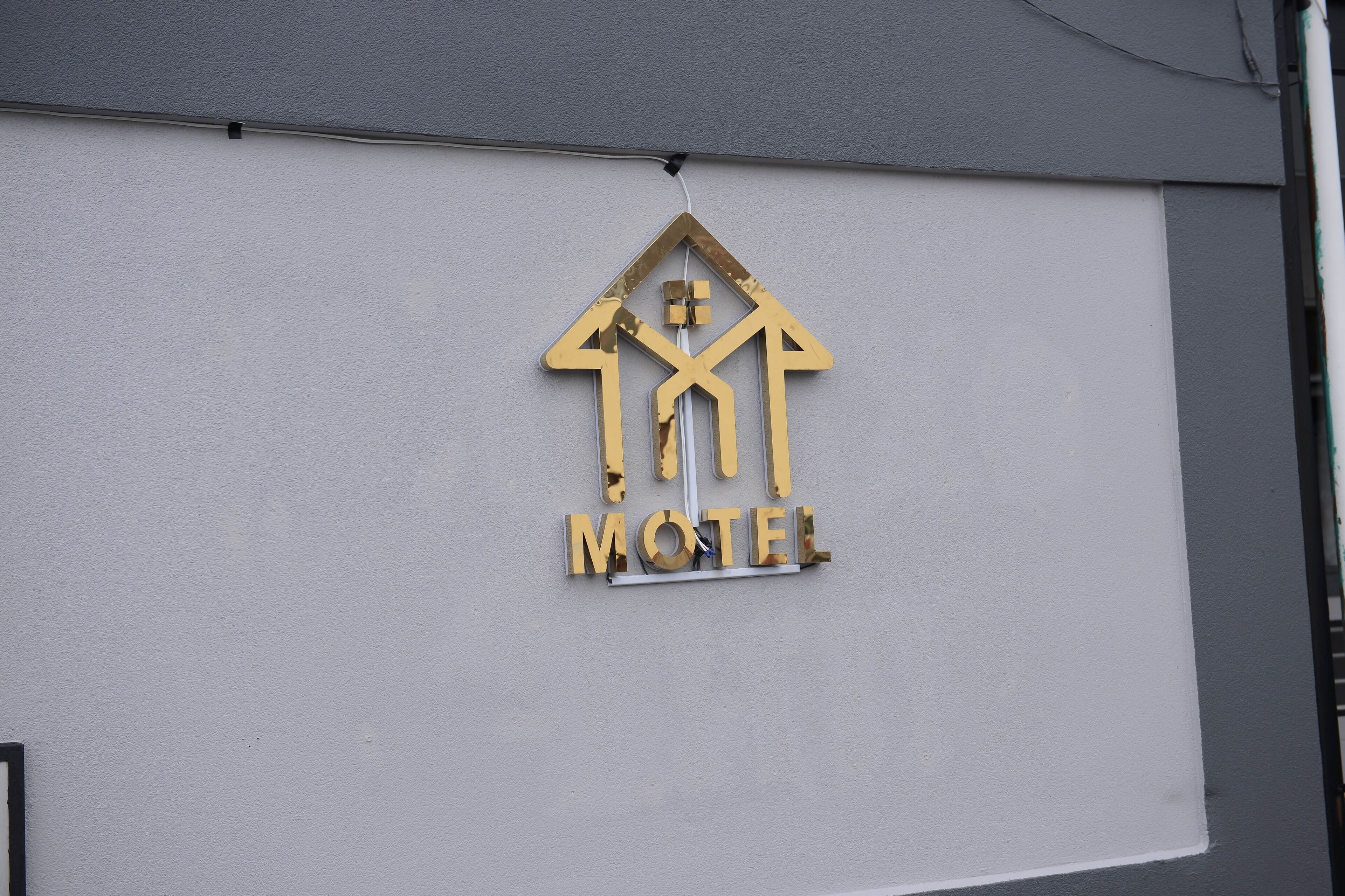 Schild eines Motels mit einem Häuschen-Symbol und dem Wort 'MOTEL' an einer weißen Wand.