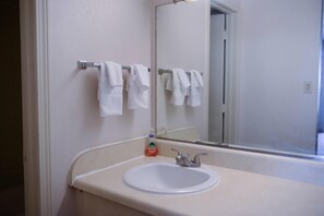 A bathroom with a white sink, a mirror, and a towel rack with several white towels.
