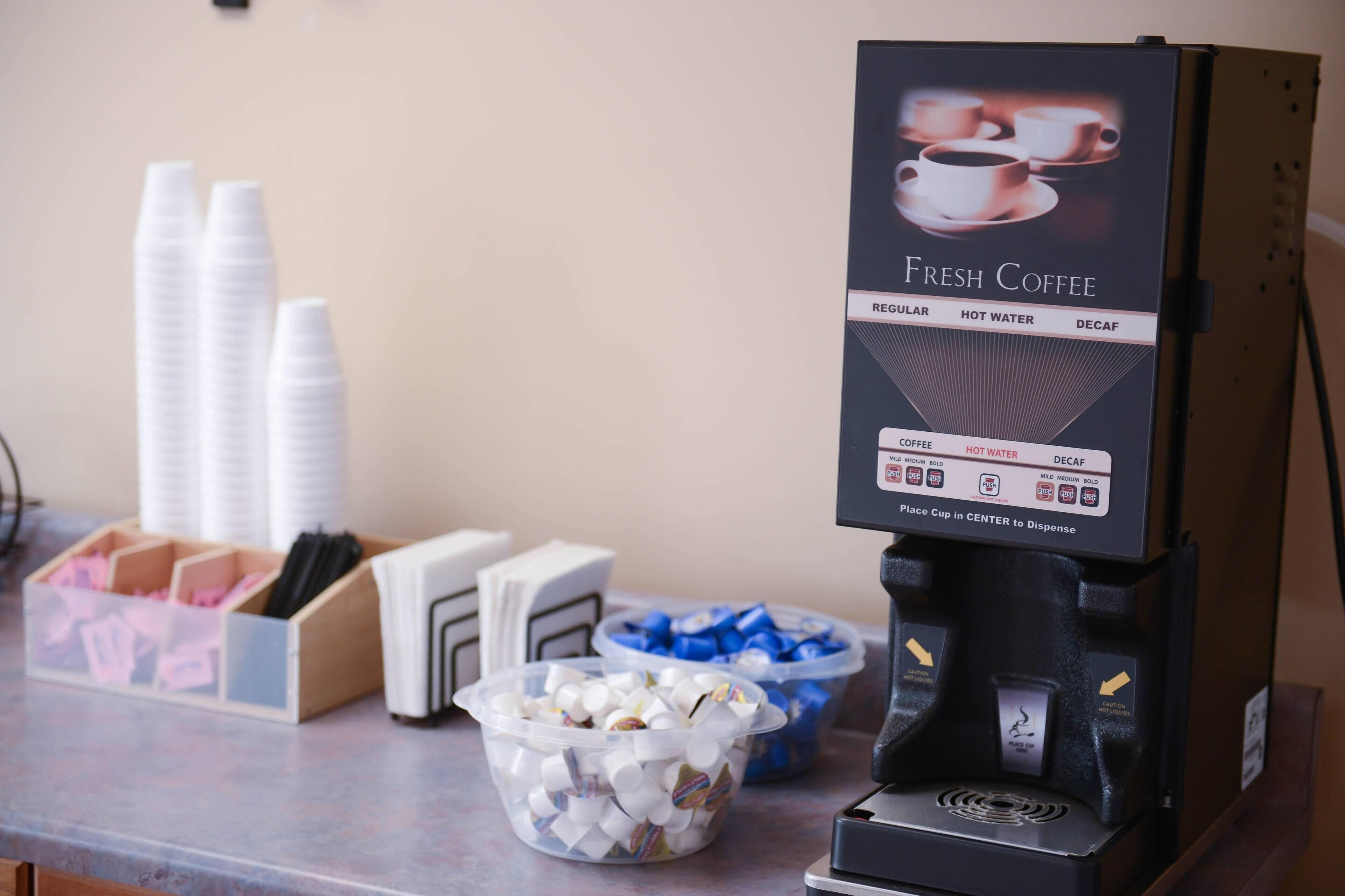 Una máquina de café con un menú que ofrece café regular, agua caliente y opciones descafeinadas, e instrucciones para colocar tazas en el centro para servir.