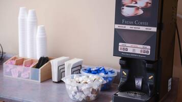 Una máquina de café con un menú que ofrece café regular, agua caliente y opciones descafeinadas, e instrucciones para colocar tazas en el centro para servir.
