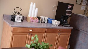 Zona de recepción de un hotel con mostrador, máquina de café y diversos servicios como servilletas, pañuelos y una planta.