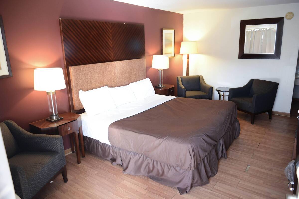 A hotel room with a large bed, two bedside tables with lamps, a chair, and a small table.