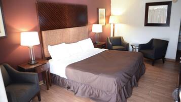 Habitación de hotel con una cama grande, dos mesitas de noche con lámparas, una silla y una pequeña mesa.