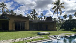 A swimming pool with a stone deck, a grassy lawn, and a building with a tiled roof and large windows.