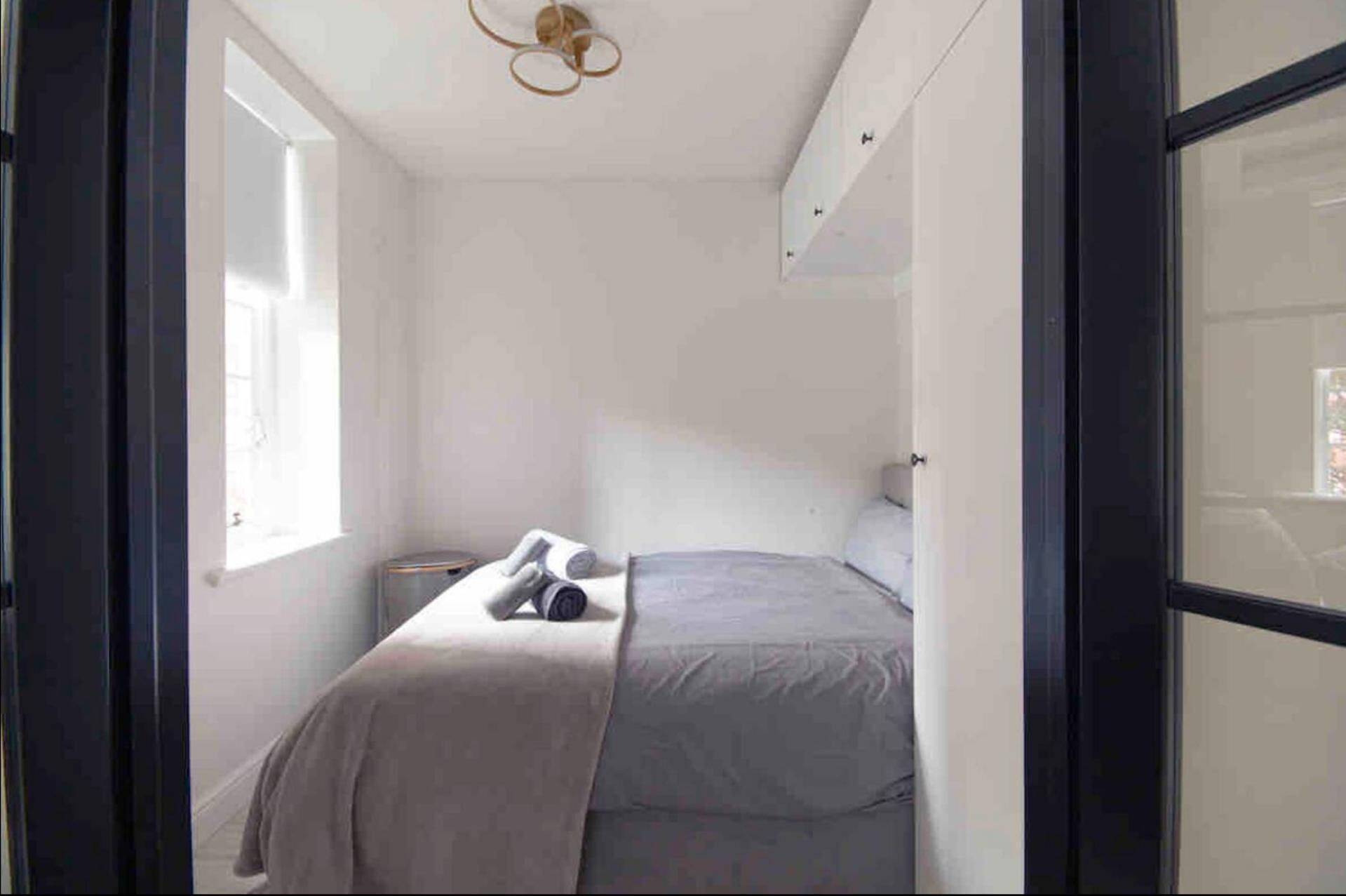 A bedroom with a bed, a nightstand, a lamp, and a window.