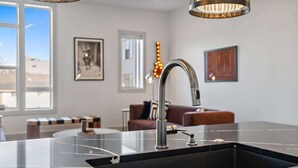 Une cuisine moderne avec un plan de travail noir et un évier en acier inoxydable. On y trouve un coin repas avec un canapé en cuir marron et une petite table.