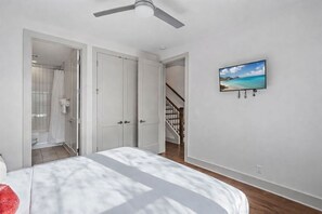 Une chambre à coucher avec un lit, un ventilateur de plafond, un téléviseur fixé au mur et un escalier menant à une salle de bain.