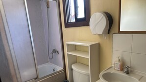 A bathroom with a shower, toilet, sink, and a small window. - Hostal Riberas del Cruces  (Mariquina)