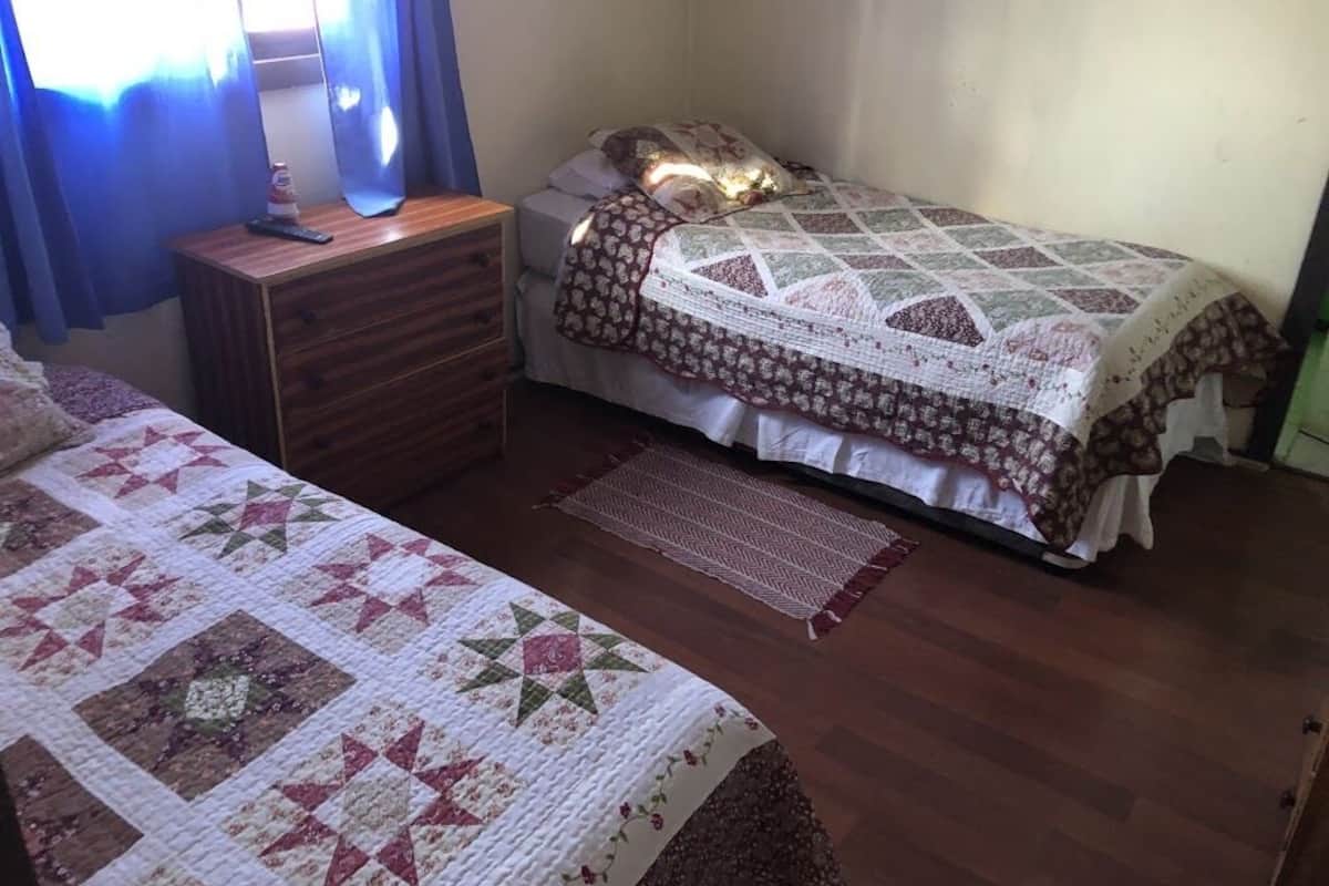 Un dormitorio con un aparador de madera, una cama con colcha y una mesita de noche con lámpara.