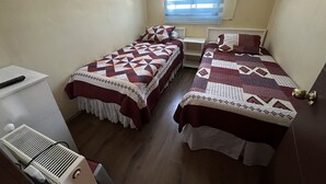A small, clean room with two beds, a window with blinds, a radiator, and a small table. - Hostal Riberas del Cruces  (Mariquina)