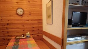 Ett rum med en träbänk, en färgglad lapptäcke, en klocka, en inramad tavla och en hylla med elektroniska apparater.
