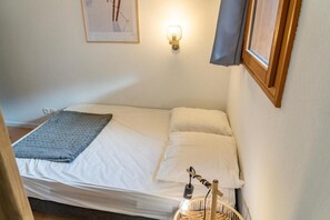 A single bed with white linens, a gray throw blanket, and a wall-mounted light fixture.