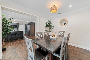 A dining area with a dark wooden table, white chairs, and a hanging light fixture. - Hard Rock Villa: Fire Pit/BBQ/Heated Pool/Jacuzzi (Miami)