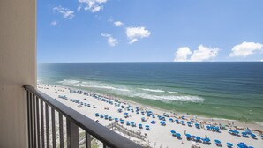 A balcony with a view of a beach with umbrellas and people. - Beachfront Resort Condo with Pools (Orange Beach)
