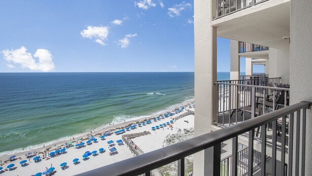 A balcony with a view of a beach with umbrellas and people. - Beachfront Resort Condo with Pools (Orange Beach)