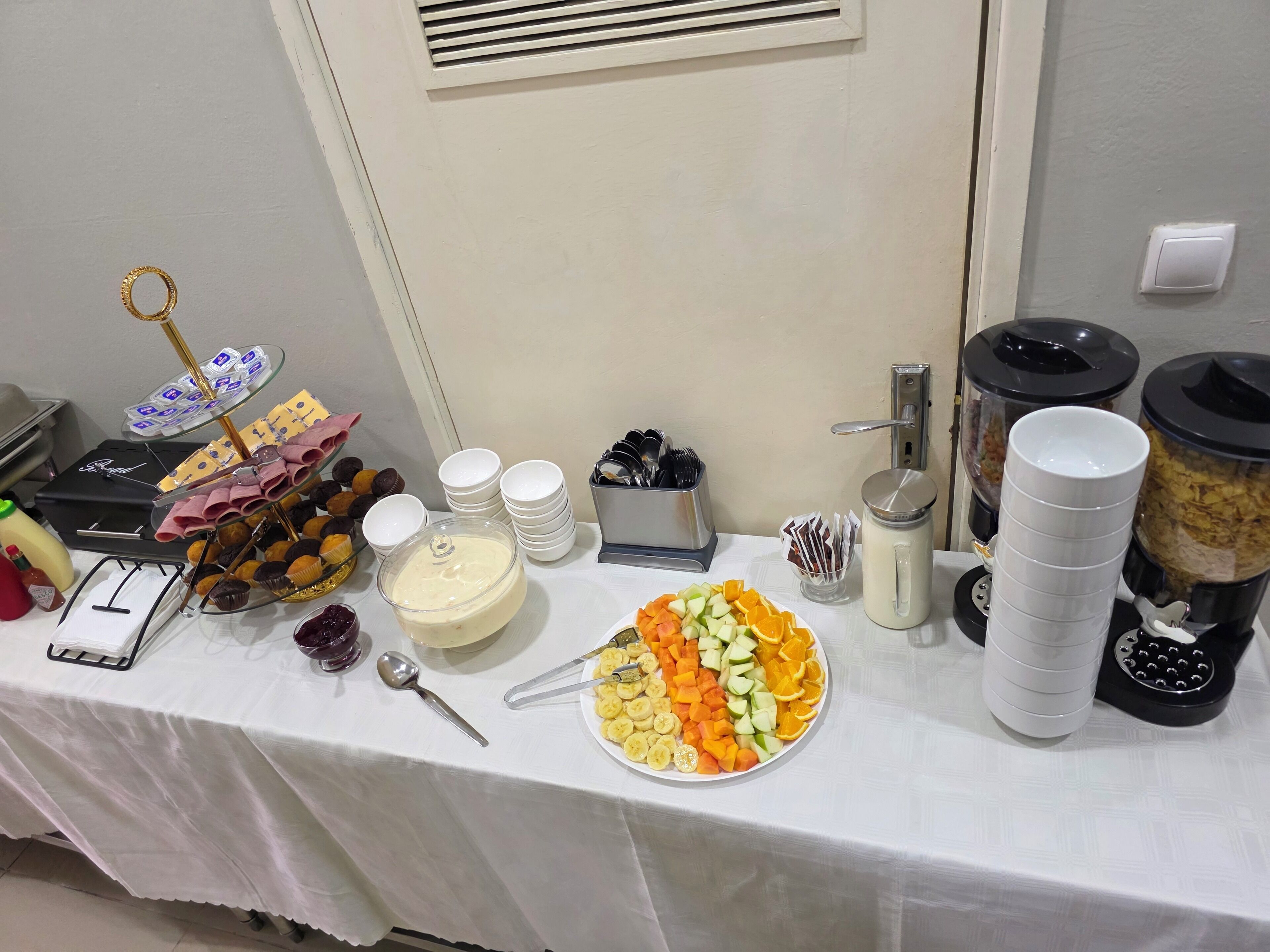 Una mesa de buffet con diferentes opciones de comida, como una bandeja de frutas, una tabla de quesos y una estación de café.