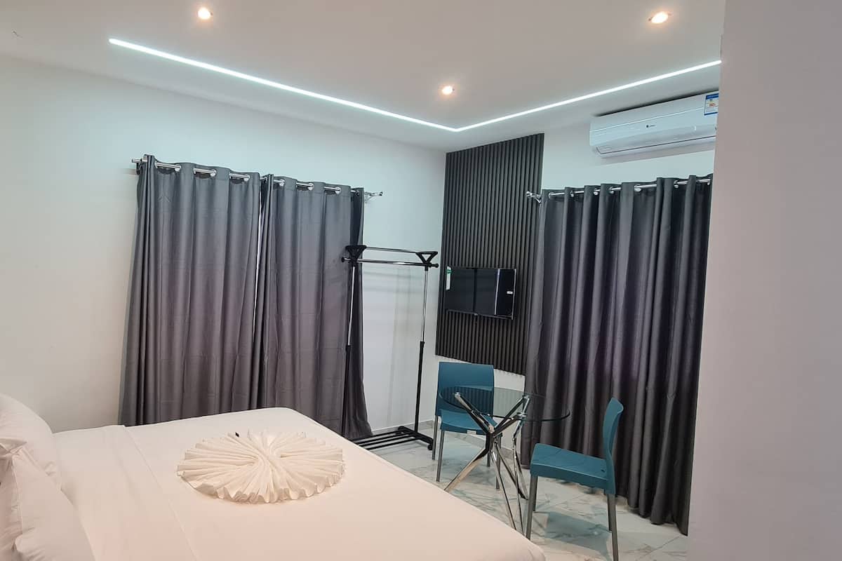 A modern hotel room with a bed, curtains, a desk with a chair, and an air conditioning unit.