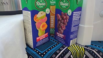 Tres cartones de mezcla de jugo Rhodes Quality Mediterranean Nectar, uno de naranja y dos de uva roja, sobre un mantel estampado.