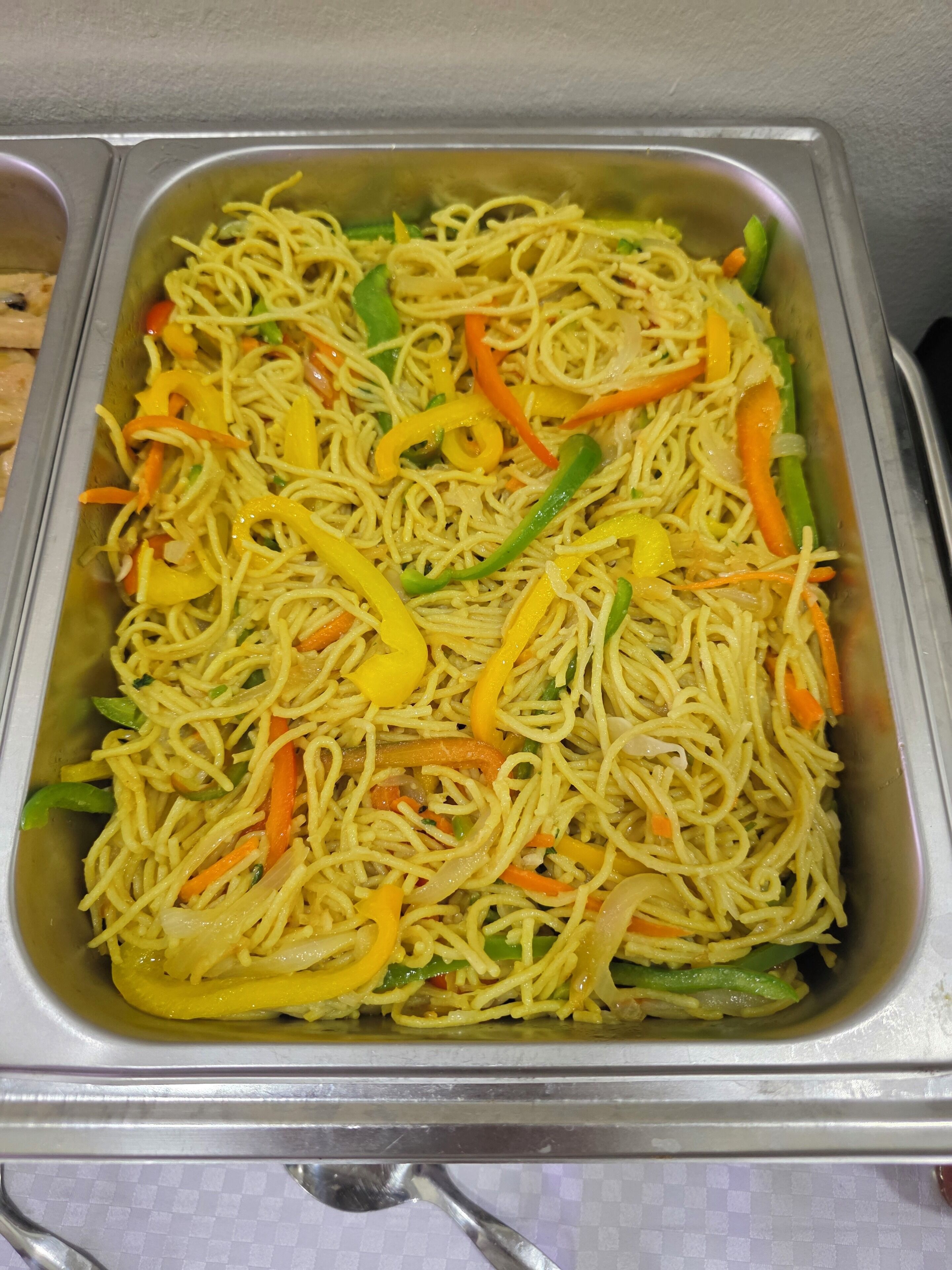 A stainless steel buffet tray filled with stir-fried noodles and vegetables.