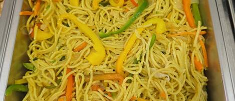 A stainless steel buffet tray filled with stir-fried noodles and vegetables.