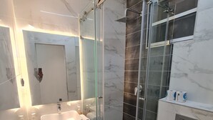 Un baño moderno con ducha de vidrio, lavamanos blanco y retrete.
