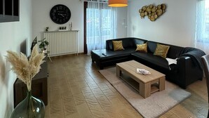 Een moderne woonkamer met een zwarte bank, een houten salontafel en een grote klok aan de muur.