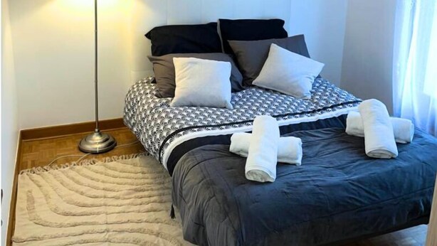 Een opgemaakt bed met een geborreld sprei, een bedlamp en een decoratieve spiegel aan de muur.