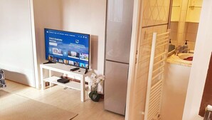Een moderne woonkamer met een flatscreen televisie, een witte bank, een klein tafeltje en een decoratieve vaas.