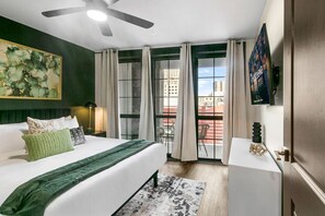 Ein Hotelzimmer mit Bett, Schreibtisch, Deckenventilator, einem Fenster mit Vorhängen und Blick auf die Stadt.
