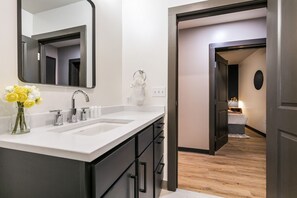 Un baño moderno con lavamanos doble, un espejo grande y un jarrón con flores amarillas.