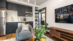 A modern kitchen with dark cabinets, stainless steel appliances, and a dining area with a grey sofa and a wooden bench. - Modern 2BR Comfort Gem Condo with 2 Balconies (New Orleans)