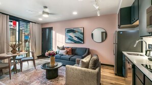 Una sala de estar moderna con un sofá, una mesa de centro y un comedor. Se observa una cocina equipada con un refrigerador y un microondas.